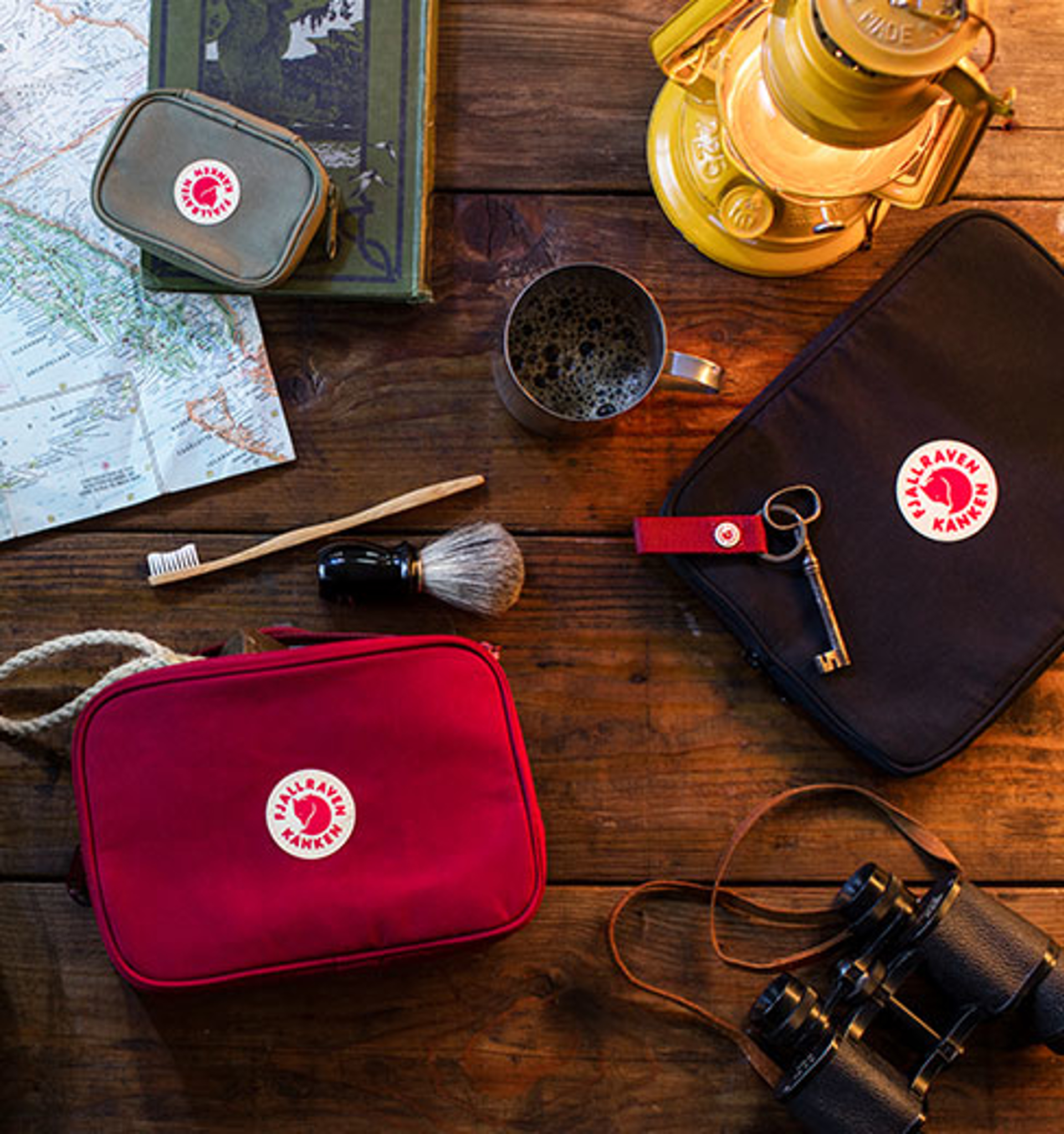 fjallraven kanken accessory bags with shaving brush, tooth brush, key, mug, lantern,  a book and a map on a table